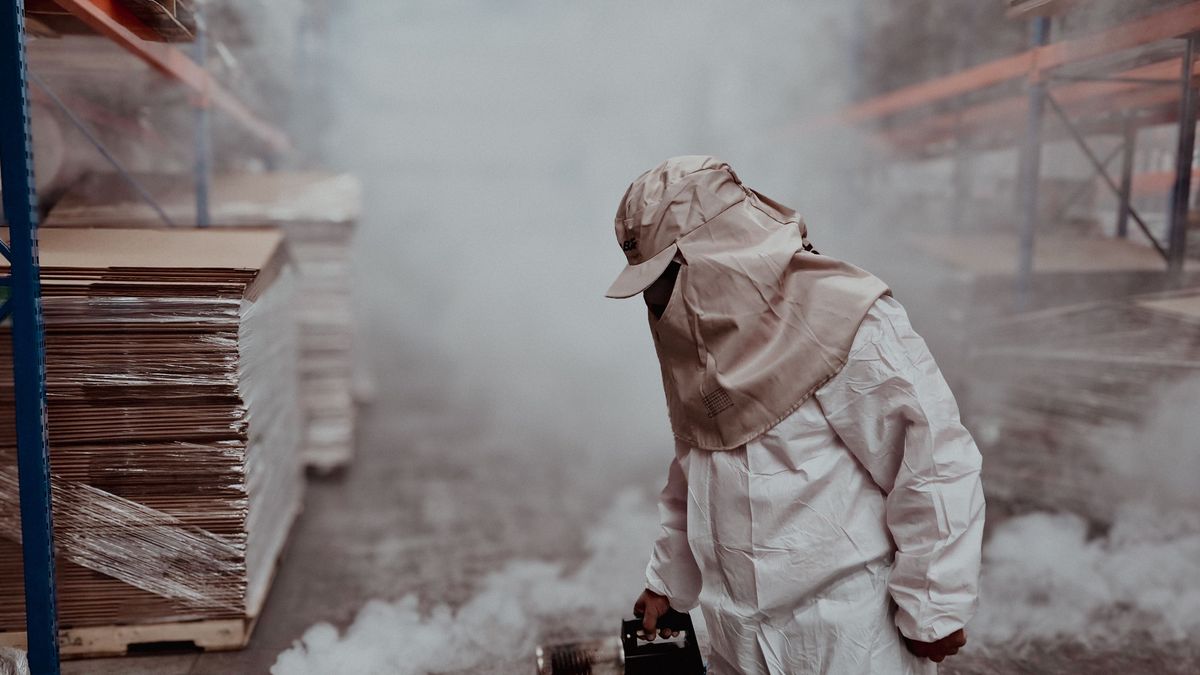 Técnico de controle de pragas com traje de proteção completo aplicando fumigação térmica em ambiente fechado
