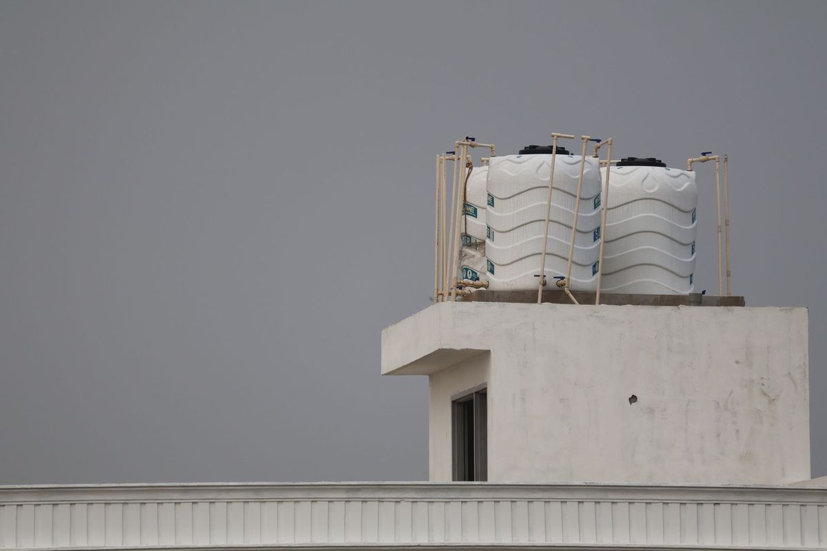 Caixas d'água plásticas brancas instaladas no telhado de um prédio, sob céu nublado