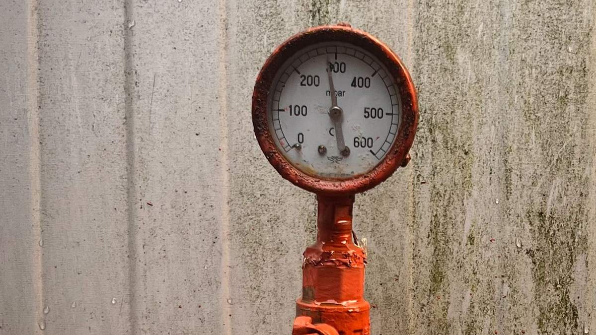 Manômetro de pressão em tom vermelho enferrujado montado em tubulação metálica, componente típico de sistema de recalque de água predial