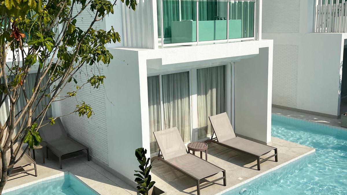 Piscina de condomínio com água azul-clara, borda de piso e área de lazer ao redor, em dia ensolarado