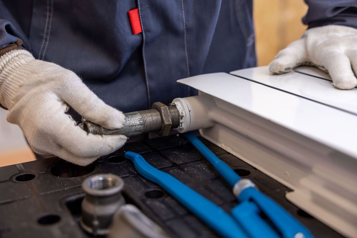 Encanador com luvas de proteção conectando uma tubulação metálica, com ferramentas de trabalho ao redor