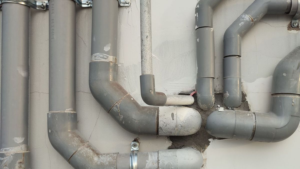 Conjunto de tubulações de PVC cinza fixadas numa parede, com conexões e joelhos aparentes